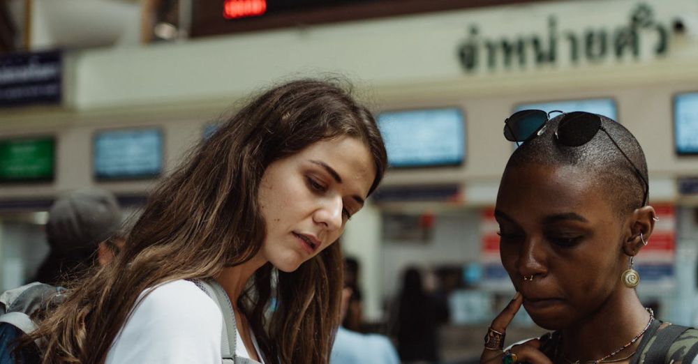 Travel Gadgets - Two women with backpacks check a train timetable at a busy station.