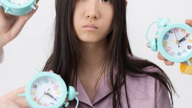 Alarm Clocks - Asian woman in pajamas with alarm clocks, illustrating insomnia concept.