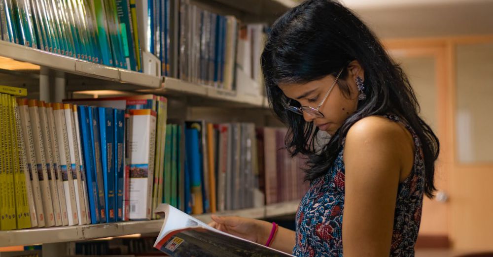 Library Memberships - College student reading a book in library.