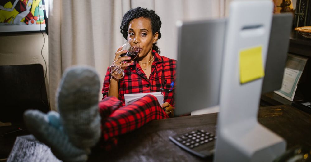 Online Courses - Woman in red pajamas relaxing with wine at a home office desk with feet up.