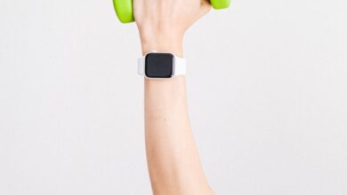 Fitness Trackers - Arm holding a green dumbbell with a smartwatch on wrist against a white background.