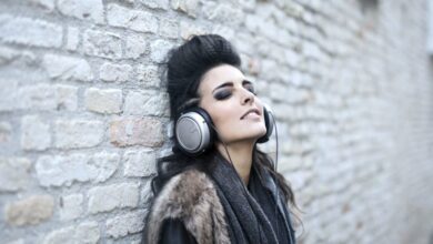 Bluetooth Headphones - Stylish young woman leaning against a brick wall, enjoying music with headphones, eyes closed in relaxation.