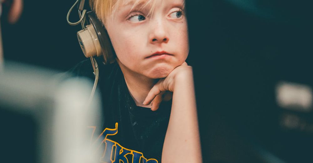 Headsets - Young blonde boy wearing headphones, focusing on a computer screen indoors.