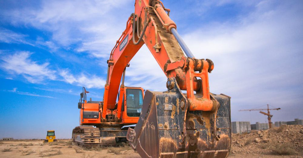 Equipment - A large orange excavator working on a construction site under a blue sky.