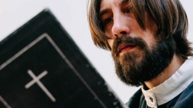 Neckbands - An adult man with long hair and beard reading a Bible indoors, emphasizing faith and spirituality.