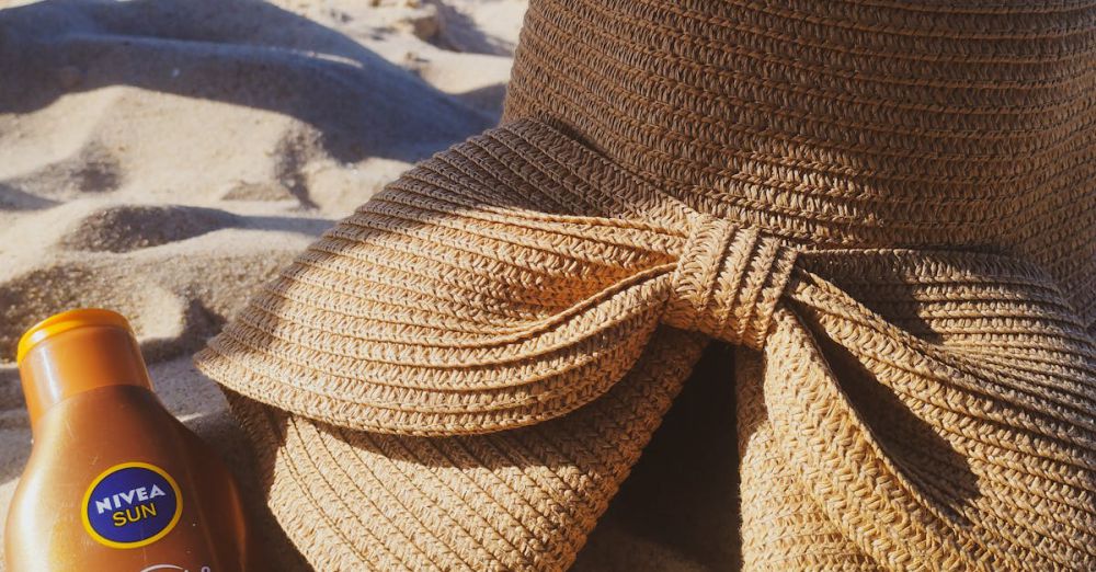 Sunscreens - A sun hat and sunscreen on a sandy beach by the ocean, perfect for summer.