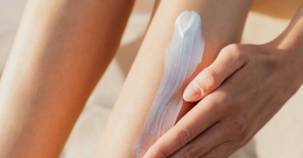 Skincare With SPF - Close-up of a woman applying sunscreen on her legs while sunbathing on a sandy beach.