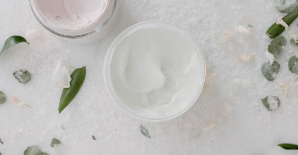 Firming Creams - Overhead shot of cosmetic cream jars surrounded by green leaves on a marble surface.