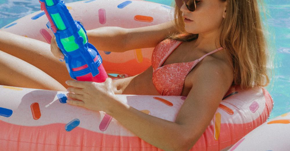 Heat Guns - Young woman in bikini enjoying pool with an inflatable donut float and water gun.