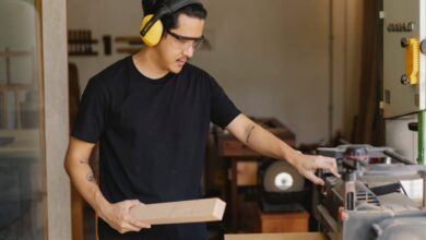 Electric Planers - Young serious ethnic male woodworker in protective headphones and glasses with timber touching electric equipment outdoors