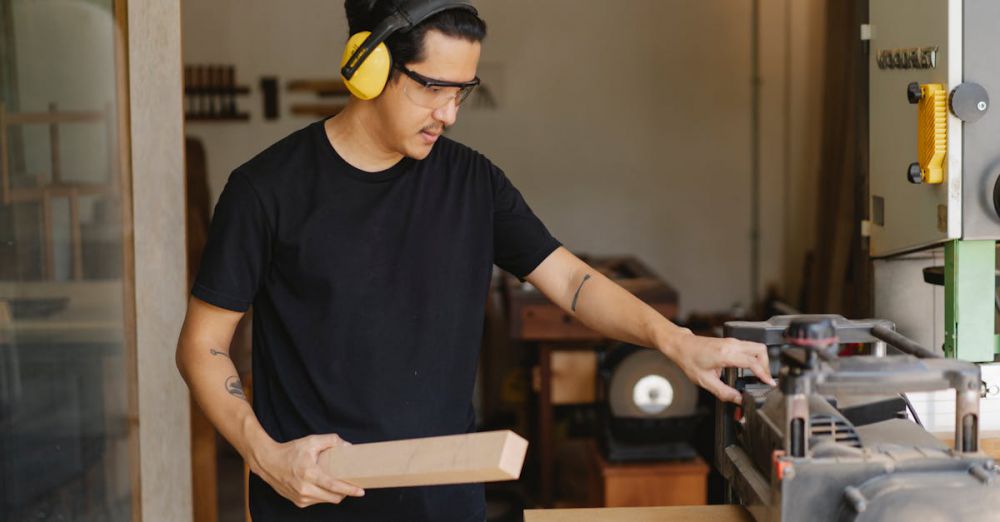 Electric Planers - Young serious ethnic male woodworker in protective headphones and glasses with timber touching electric equipment outdoors