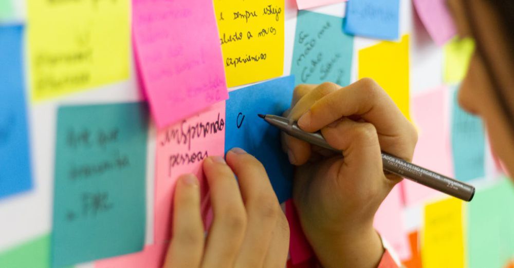 Sticky Notes - Hands writing on colorful sticky notes during a brainstorming session indoors.