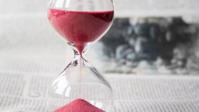 Time - Close-up of a transparent hourglass with pink sand flowing, placed on a newspaper background.