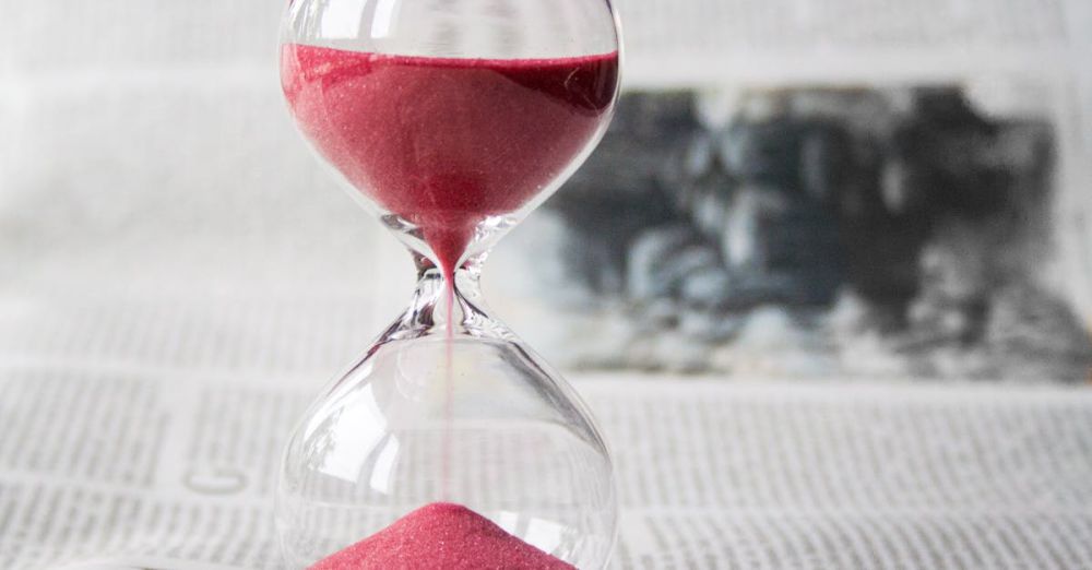 Time - Close-up of a transparent hourglass with pink sand flowing, placed on a newspaper background.