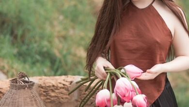 Wear - An elegant young woman holding pink tulips in a serene outdoor setting, embodying natural beauty and tranquility.