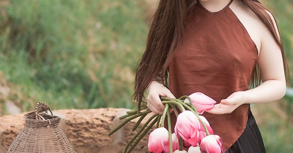 Wear - An elegant young woman holding pink tulips in a serene outdoor setting, embodying natural beauty and tranquility.