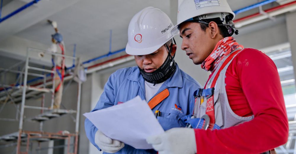 Safety - Two engineers in safety helmets reviewing construction plans at a worksite.