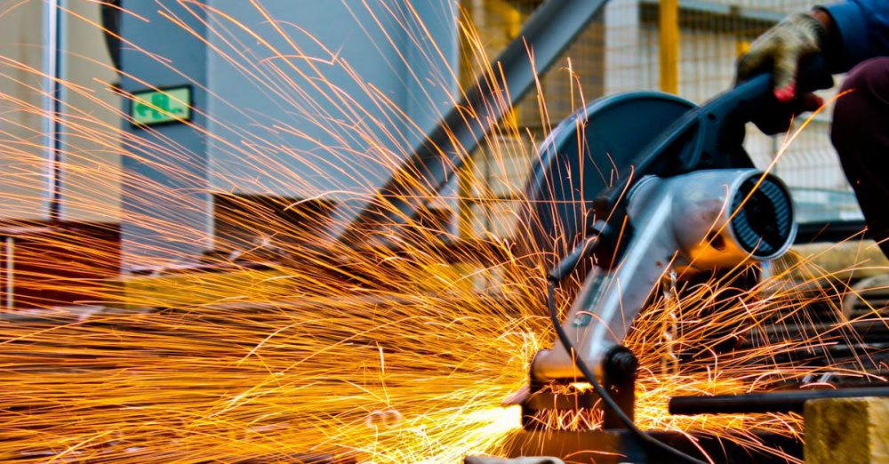 Equipment - A worker operates a grinder cutting metal, creating a vibrant display of sparks in an industrial setting.