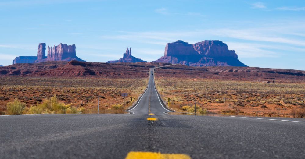 Distance - A straight highway leads through the iconic Monument Valley under a clear blue sky.