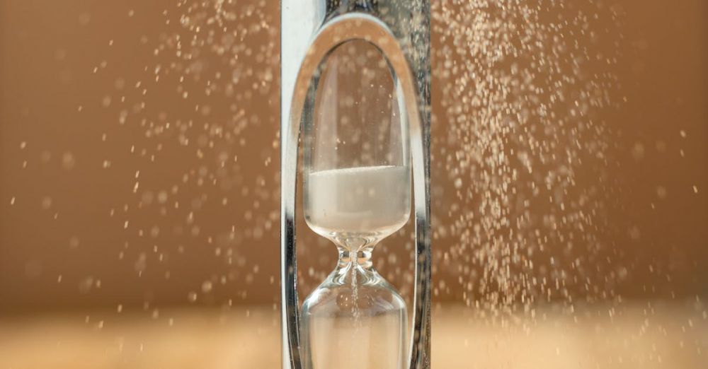 Duration - Close-up of an hourglass with sand falling, capturing the essence of time against a yellow background.