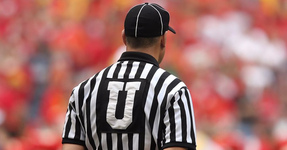 Rules - A football umpire in uniform overseeing the game in a crowded stadium.