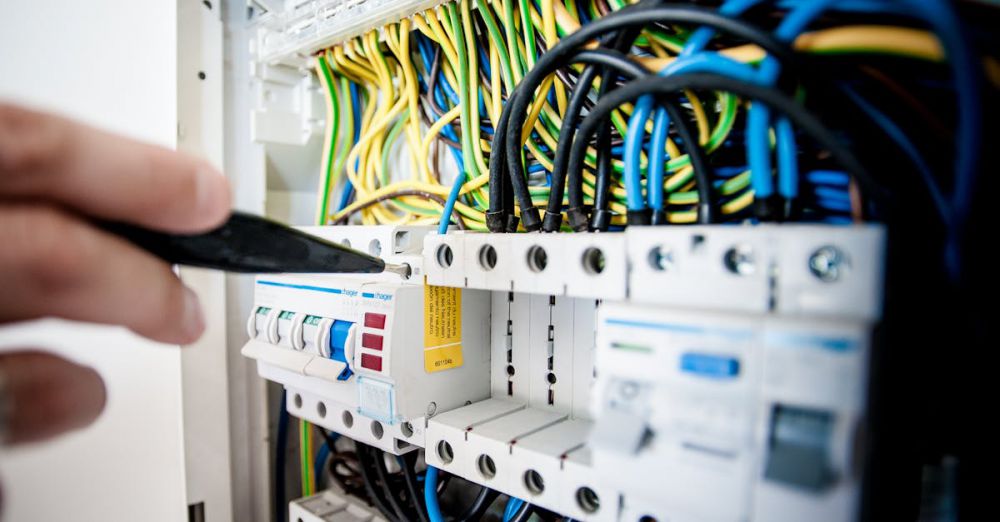 Equipment - Hand of electrician working on a circuit breaker panel with colorful wires, ensuring safe electrical connections.