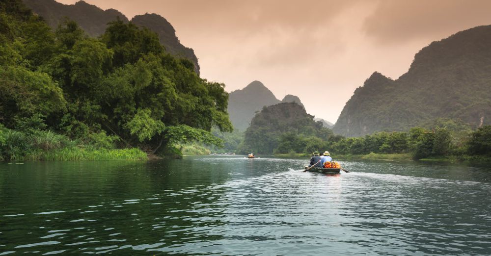 Tours - Two people rowing a boat through a serene river surrounded by lush greenery and mountains.