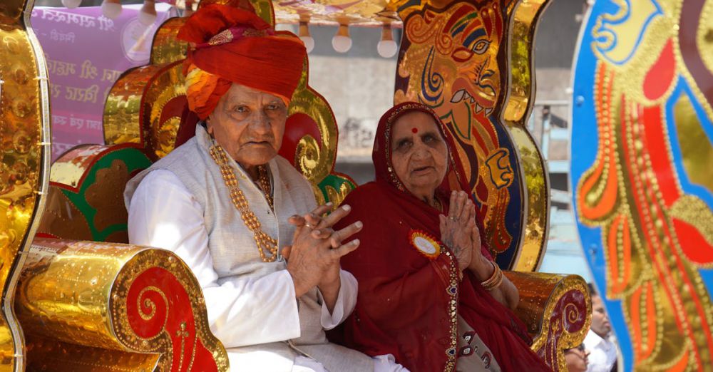 Cultural Significance - Elderly couple in colorful Indian attire sitting on a decorated ceremonial seat at a festival.