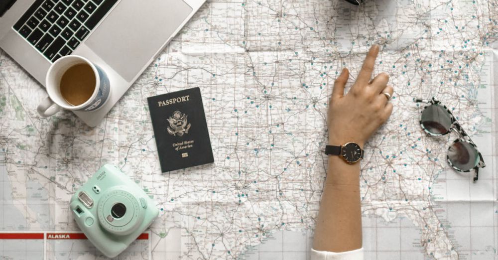 Trip Planning - Hand on map with camera, passport, laptop, and coffee, perfect for travel planning inspiration.