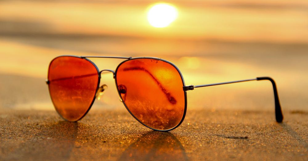 Summer - Close-up of sunglasses on a beach during a vibrant sunset, capturing the essence of summer.