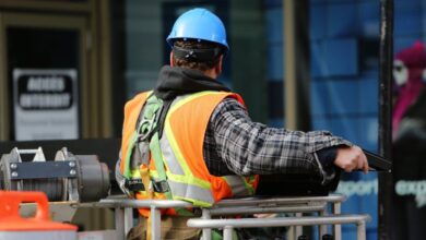 Safety - A construction worker wearing a blue helmet and safety vest operates equipment at an urban construction site.