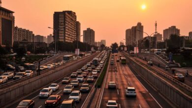 Transportation - A bustling urban highway with heavy traffic under a vibrant sunset sky against a cityscape backdrop.