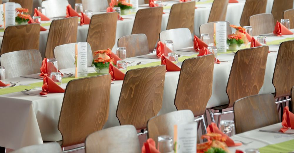 Events - Beautifully arranged tables with wooden chairs for a formal event, adorned with orange flowers.