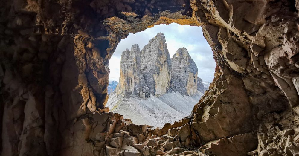 Year-Round Hiking - A breathtaking view of the Dolomites seen through a natural cave opening.