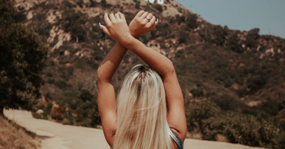 Popular Trails - Blonde woman in blue swimsuit posing with arms raised in front of the iconic Hollywood sign.