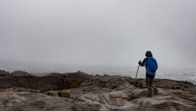 Challenging Trails - A lone hiker explores a foggy, rocky landscape with a glacier view, embodying adventure.