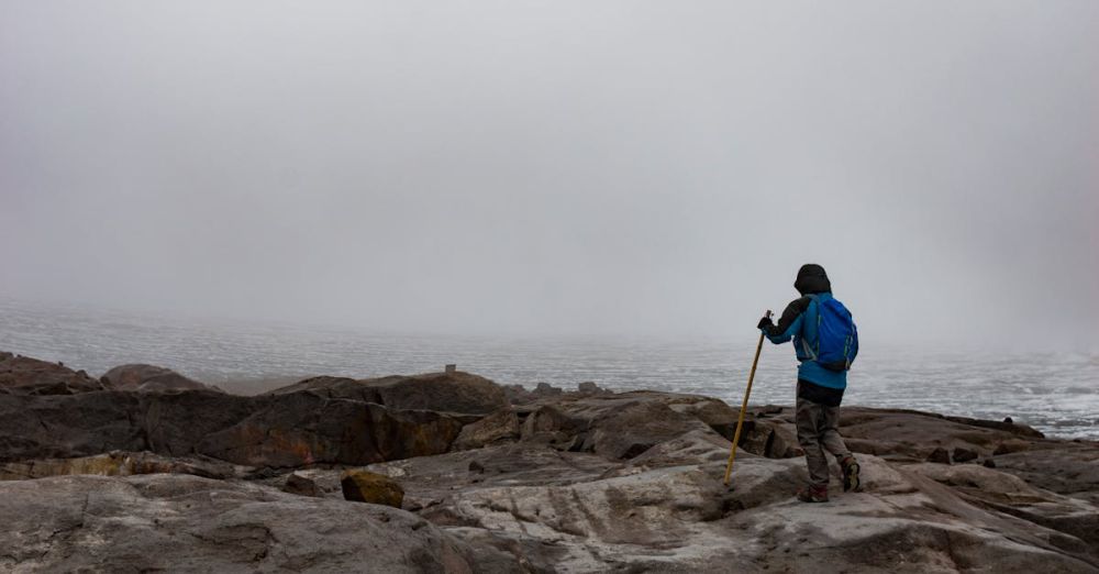 Challenging Trails - A lone hiker explores a foggy, rocky landscape with a glacier view, embodying adventure.