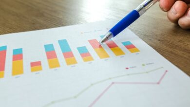 Preparation - Detailed close-up of a hand pointing at colorful charts with a blue pen on wooden surface.