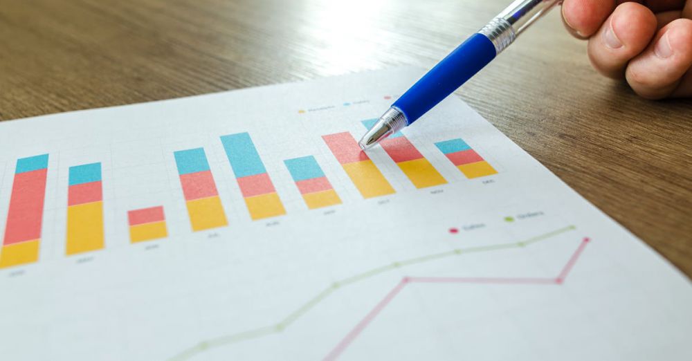 Preparation - Detailed close-up of a hand pointing at colorful charts with a blue pen on wooden surface.