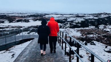 Winter Trails - Two individuals walk on a snow-covered footbridge in a cold, scenic landscape.