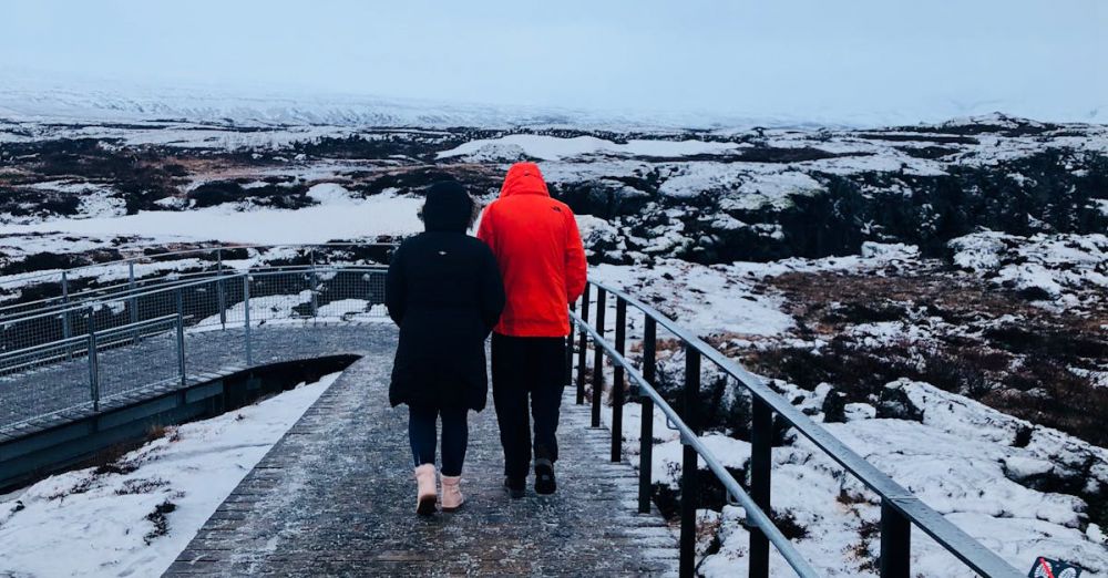 Winter Trails - Two individuals walk on a snow-covered footbridge in a cold, scenic landscape.