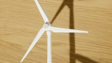 Energy - Close-up of a hand holding a small wind turbine model casting a shadow on a wooden surface.