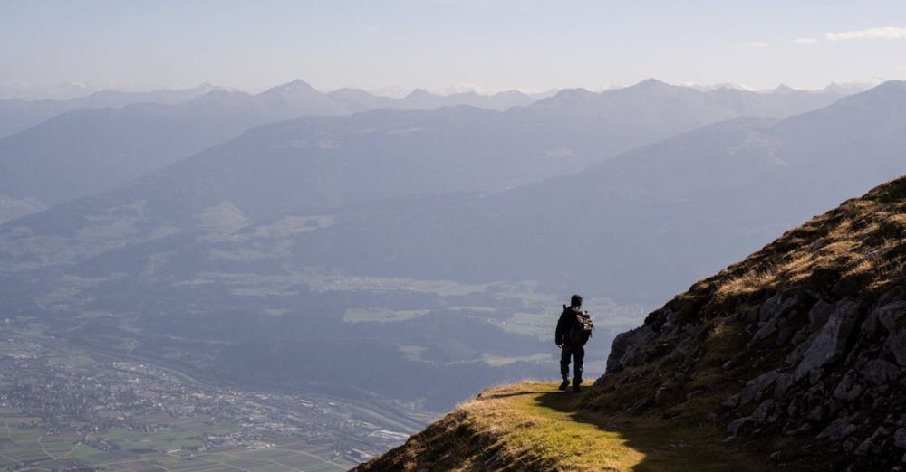 Solo Hiking - A lone hiker stands on a mountain path overlooking the vast Austrian Alps near Innsbruck.