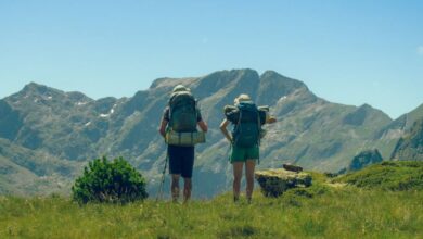 Experienced Hikers - Two hikers with backpacks enjoying a mountain view under a clear sky.