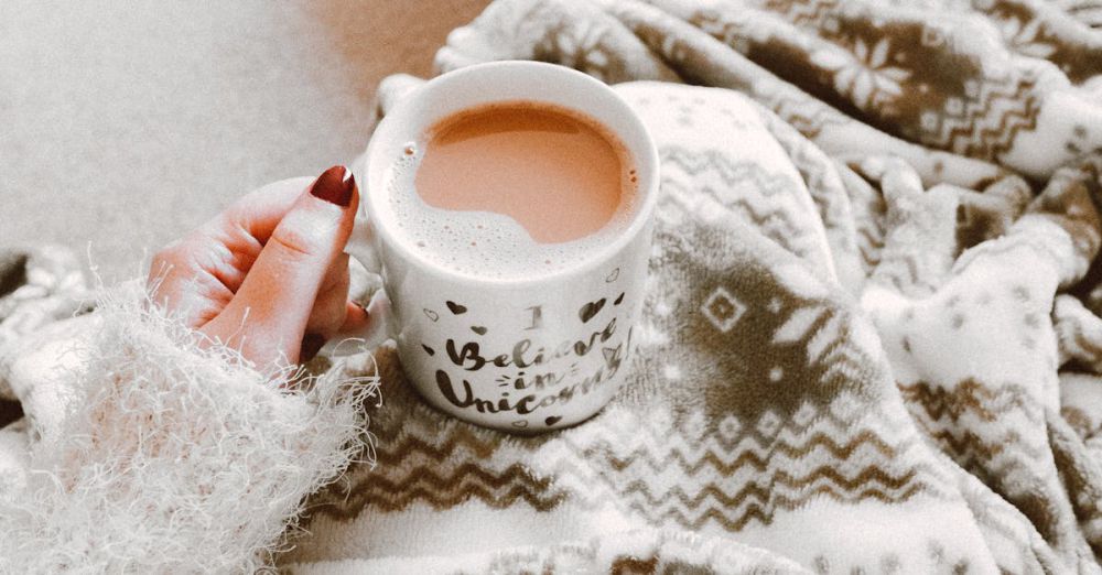 Comfort - Person holding a hot drink surrounded by cozy blanket indoors. Perfect for winter comfort.