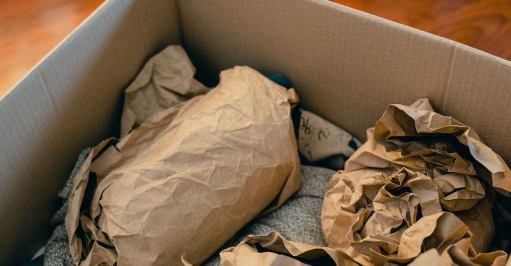 Packing - From above of open cardboard box on wooden floor full of things wrapped in packaging paper prepared for moving in new apartment