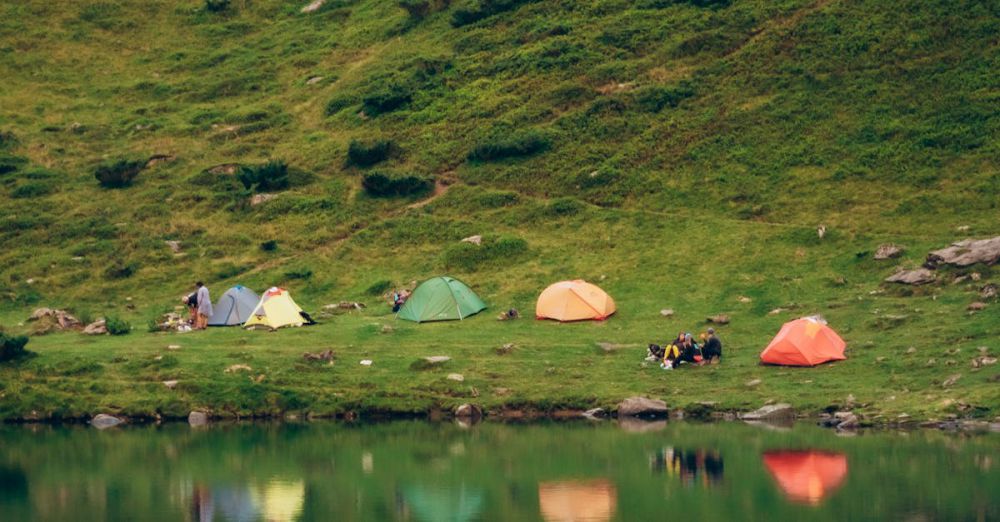 Tent Camping - A serene view of colorful tents by a mountain lake, ideal for camping enthusiasts.