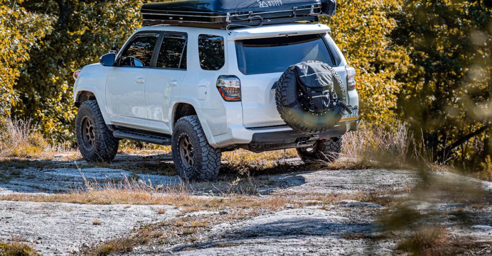 Scenic Camping - White SUV parked on a rocky terrain in a forested area, showcasing outdoor adventure.