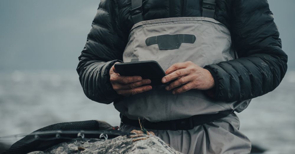 Fishing - Man in protective clothing using tablet with gloves in cold, misty outdoor setting. Ideal for tech and outdoor adventure themes.