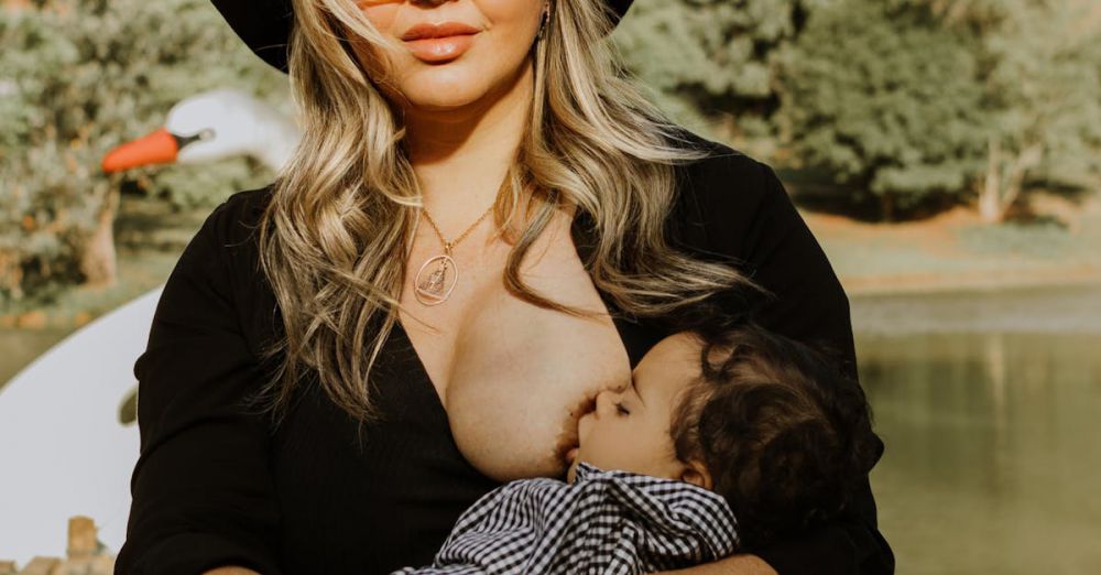 Year-Round Camping - A mother in cowboy attire breastfeeding her baby by a serene lake outdoors.